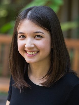 A woman with brown hair and black shirt smiles for a photo
