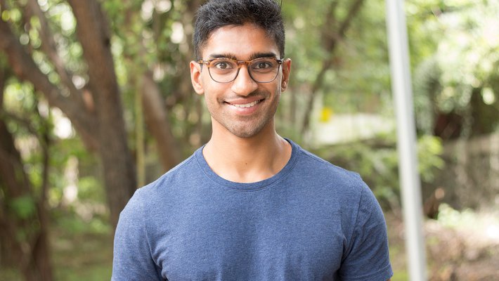 A portrait of Eshaan Patheria. He wears glasses and a T-shirt and smiles at the camera.