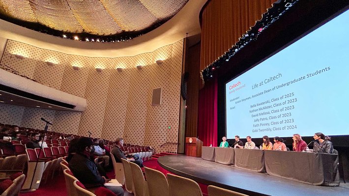 Parents in the first two rows of an auditorium look to the stage, where a panel of students sit in front of a screen that says "Life at Caltech"
