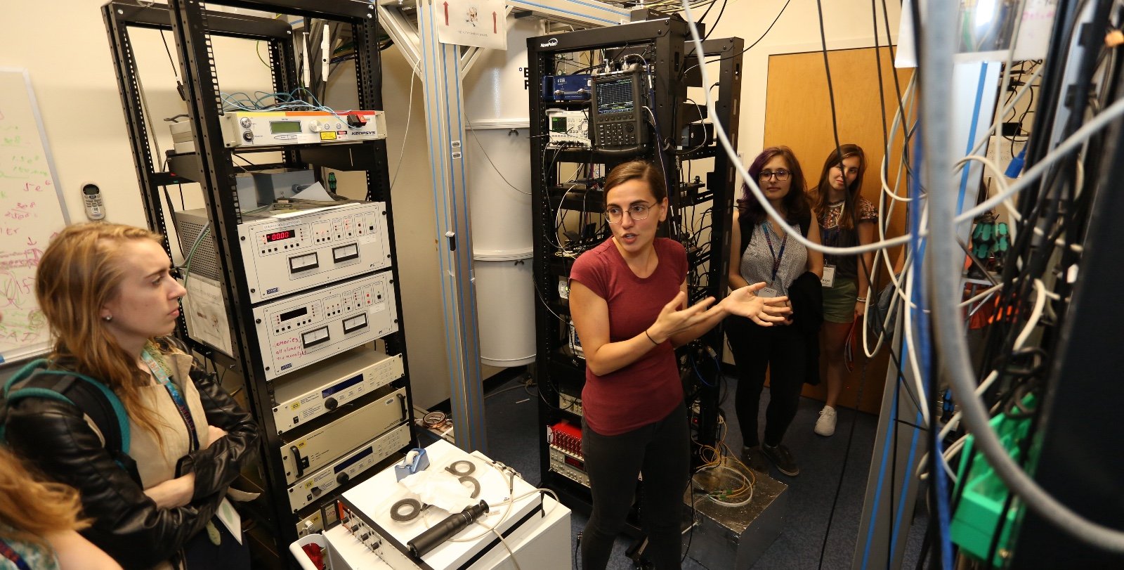 A scientist is seen talking to others in a lab full of equipment. 
