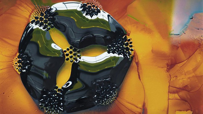 photo of a 2-cm drop of ferrofluid, placed on a glass slide, under which are seven circular magnets.
