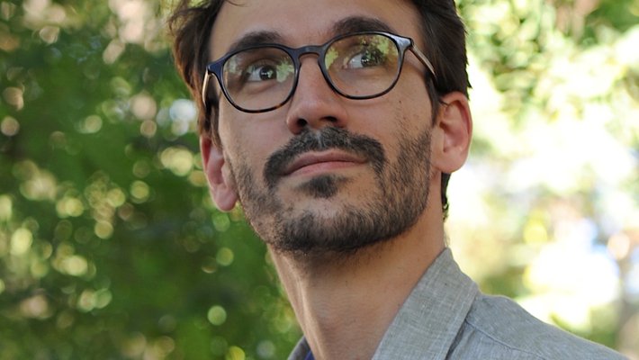 Headshot of a man with dark hair and glasses and a gray collared jacket.