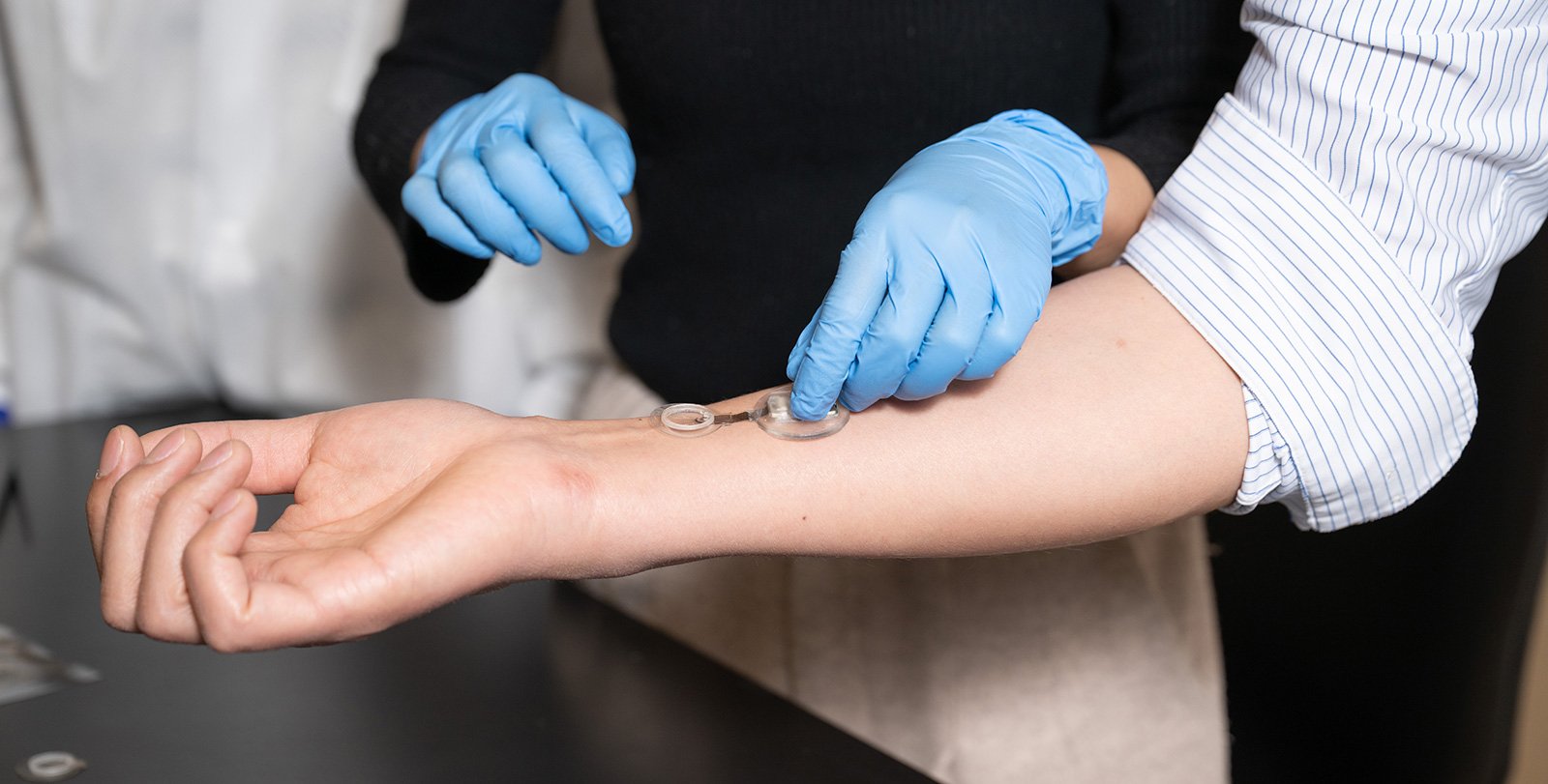 someone wearing blue plastic gloves applying a smart bandage on another person's outstretched forearm