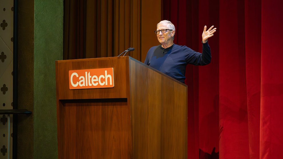 Bill Gates, smiling and gesturing, stands behind a podium with Caltech's logo