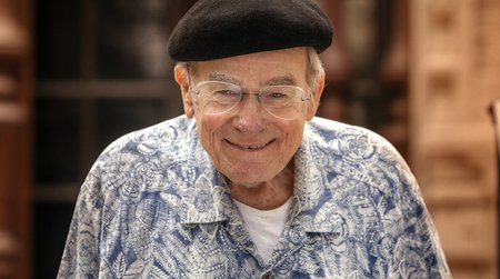 photo of a smiling man with a Hawaiian style shirt, glasses, and a black beret