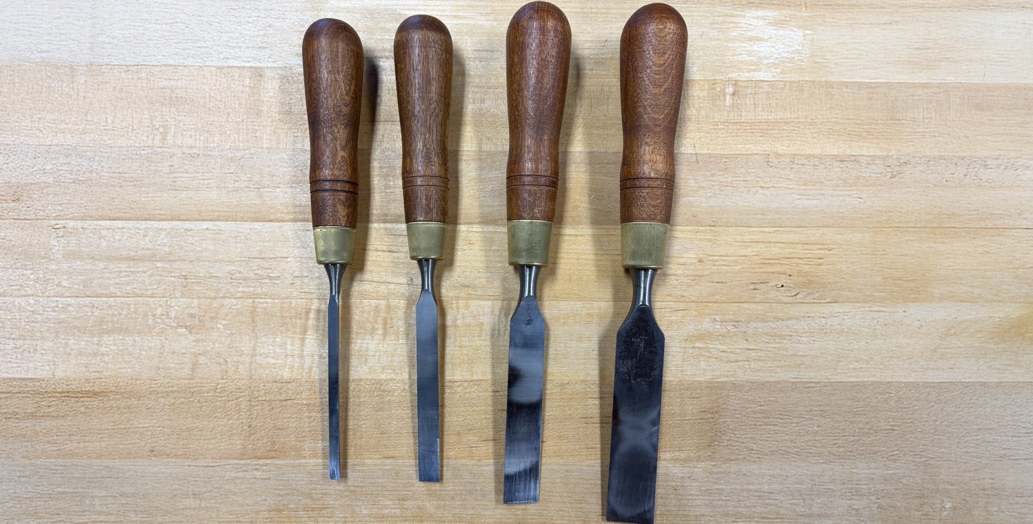 Four chisels with wooden handles lie side-by-side on a wooden table