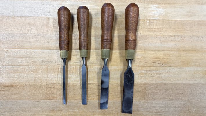 Four chisels with wooden handles lie side-by-side on a wooden table