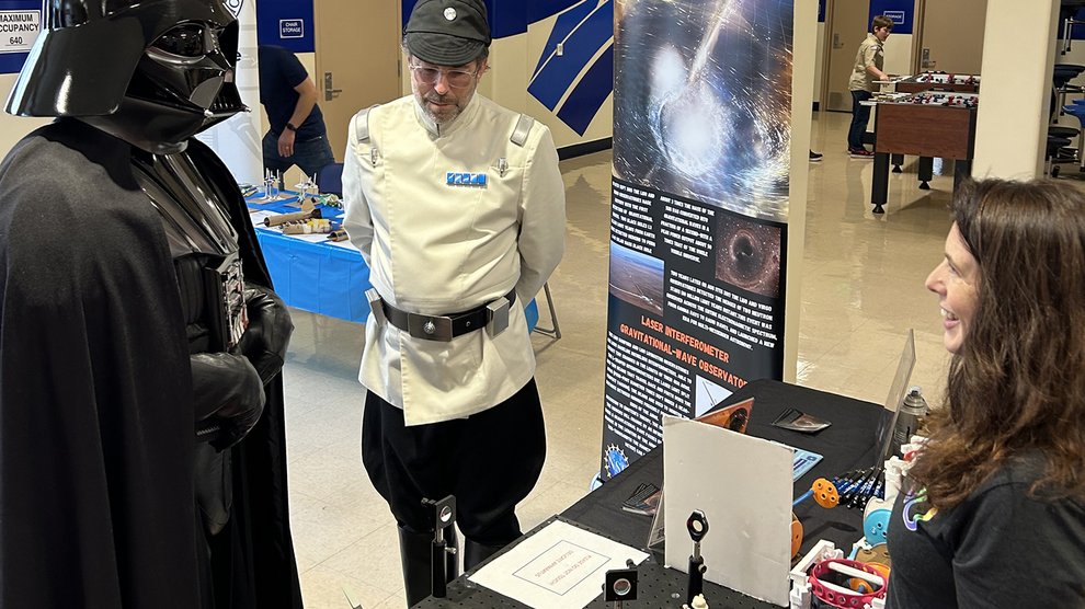 Two people costumed as Star Wars characters speak with Lorna Campbell at an exhibit about the LIGO observatories