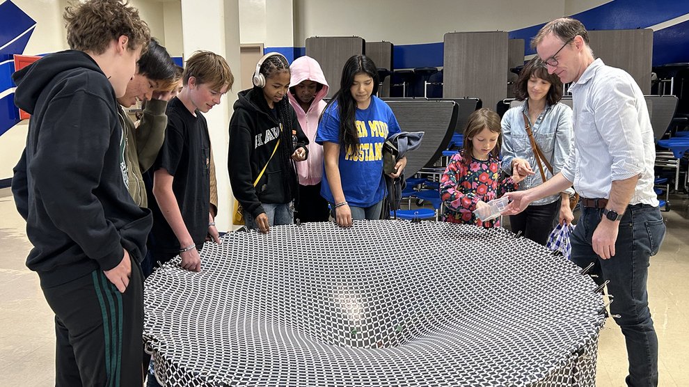 Several people roll marbles into a round stand draped with fabric that drops toward the center