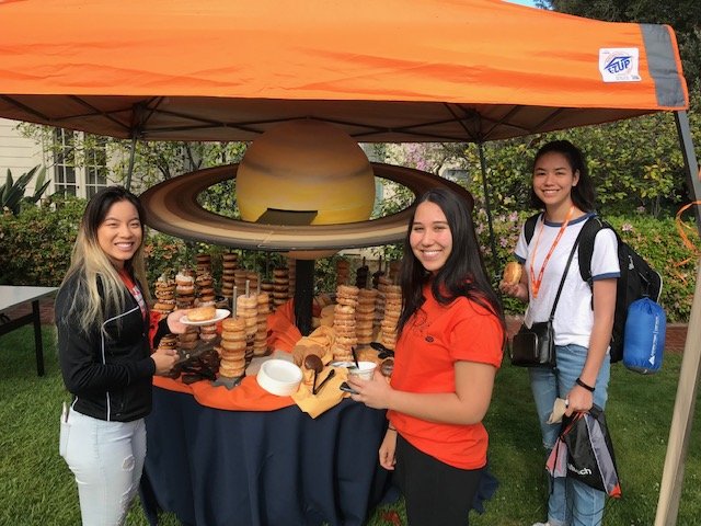 Students next to a table of donuts arranged like the planet saturn.