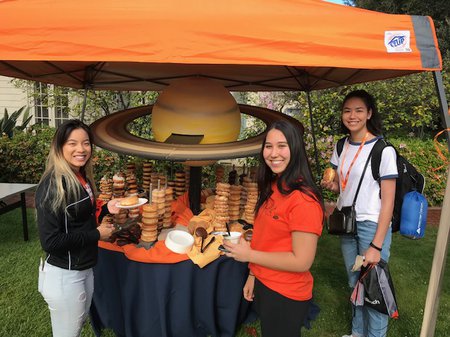 Students next to a table of donuts arranged like the planet saturn.