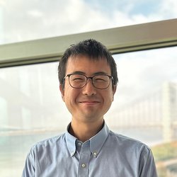 A photo of Kiyohito Iigaya. He wears a button-down shirt and glasses and smiles at the camera..