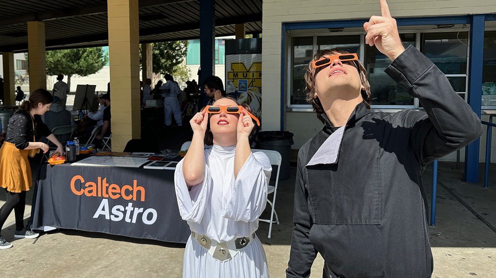 People dressed as Princess Leia Organa and Luke Skywaker and wearing eclipse glasses stare into the sky