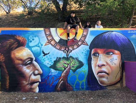 mural painting on a wall with an indigenous man, a tree, the sun above, and an indigenous girl