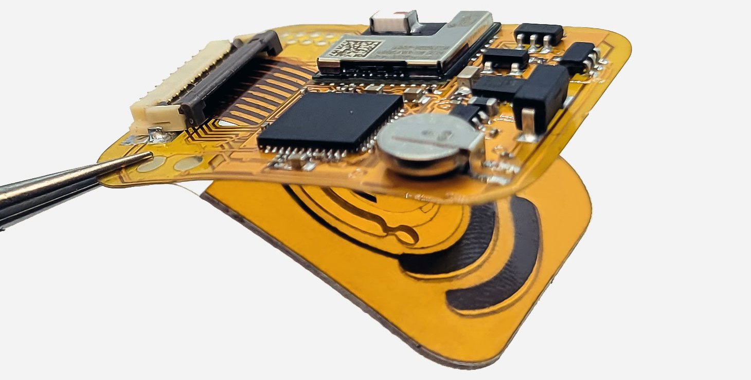 Tweezers hold a small electronic device made on a flexible film. There are various components attached to the film.