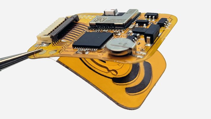 Tweezers hold a small electronic device made on a flexible film. There are various components attached to the film.