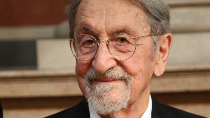 A portrait of Martin Karplus, an older man wearing a dark suit and red tie.