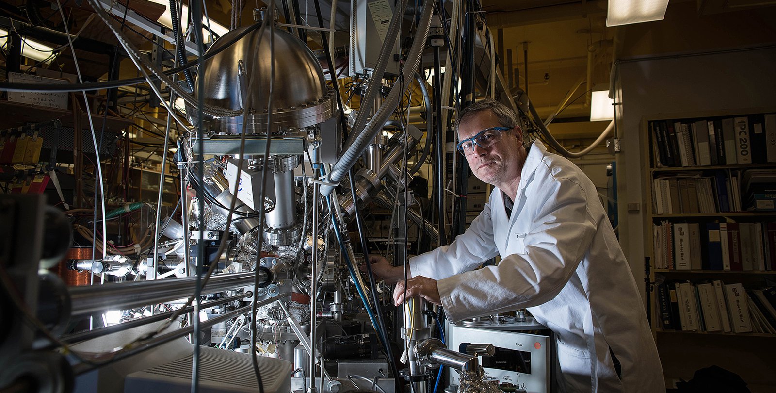Konstantinos Giapis stands in front of his oxygen reactor. It appears as a complex tangle of tubes and wires.