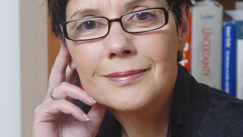 A portrait of Diana Kormos Buchwald. She smiles at the camera in front of a book case.