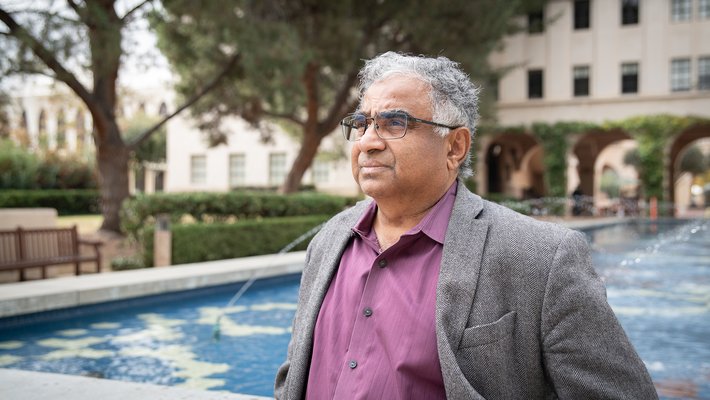 Image of Shri Kulkarni in purple shirt and grey blazer in front of fountain