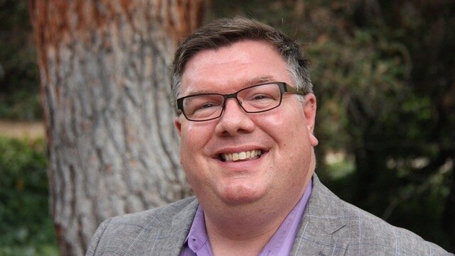 Portrait of Lee Coleman in front of a tree smiling in collared shirt and jacket