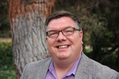 Portrait of Lee Coleman in front of a tree smiling in collared shirt and jacket