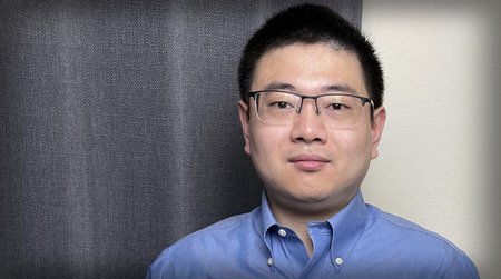 A portrait of Lei Li, who stands in his office wearing a button-down shirt and glasses.