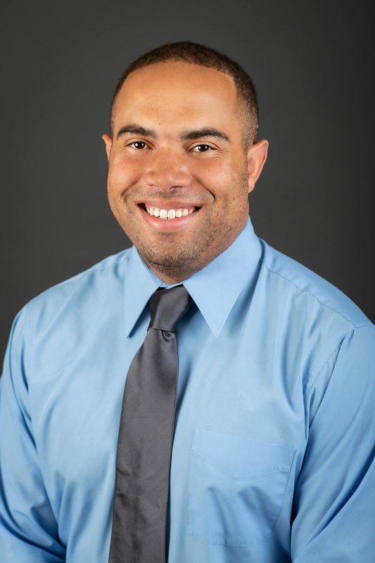 A man in a shirt and tie smiling for a photo