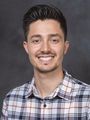 A man with dark hair and plaid shirt smiles for a photo