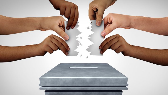 Six arms reach out to hold a ballot that is being ripped in two above a ballot box