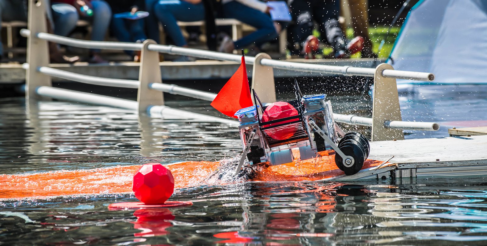 A robot splashes through Millikan Pond with a brightly-colored ball it has captured.