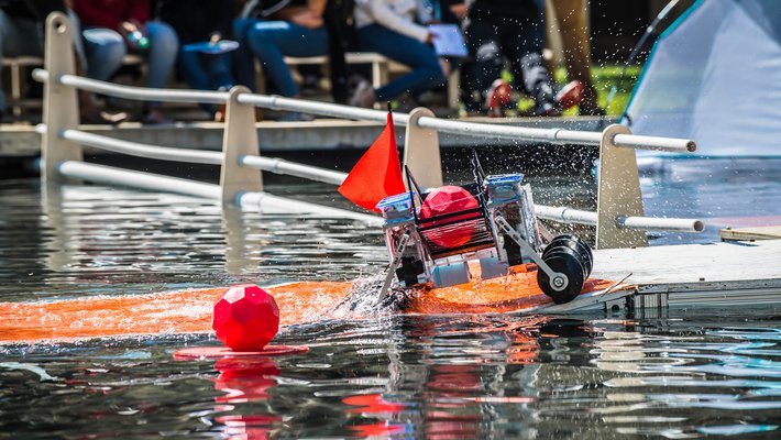 A robot splashes through Millikan Pond with a brightly-colored ball it has captured.