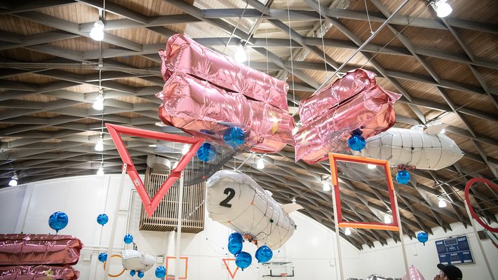 This is a picture of large metallic balloon blimps in a student competition soaring above a basketball court, trying to push blue neutrally buoyant balls through goals 10 feet up in the air.