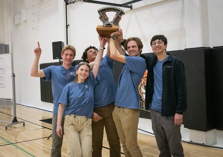 Five students in blue shirts hold up the gear trophy that goes to the ME72 champions each year.