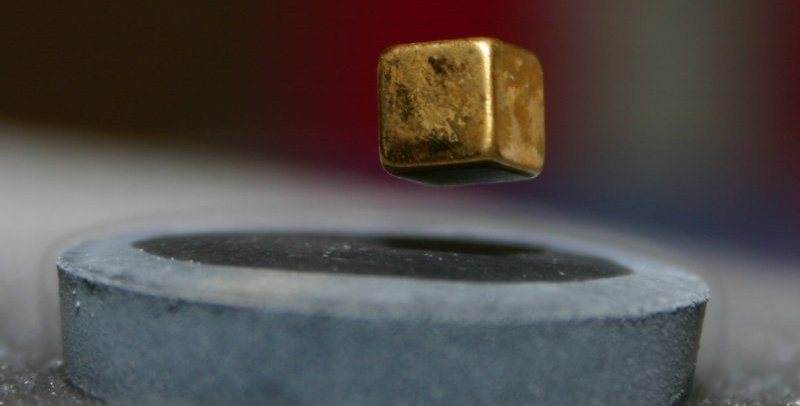 A small magnet levitates above a piece of high-temperature superconductor. The magnet is cube shaped. The superconductor is covered in frost and surrounded by wisps of vapor.