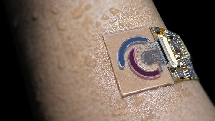 A human arm covered with droplets of water has a small sensor attached to it. The sensor is a clear membrane with sectors and wires.