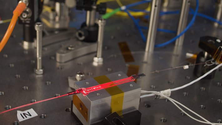 A red laser light shines through a flat waveguide on a metal workbench.