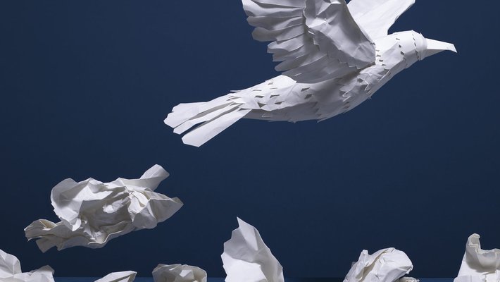 a white bird made of paper flying over crumpled papers