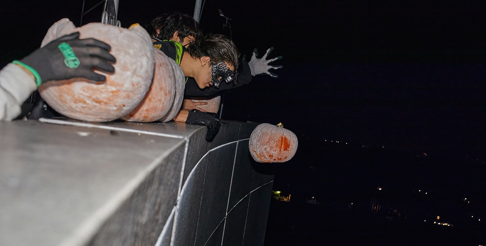 Masked woman drops a pumpkin from atop a building