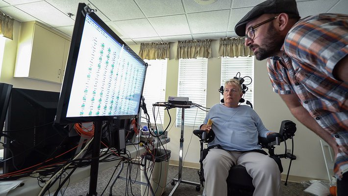 A man and a woman in a wheelchair examine a screen