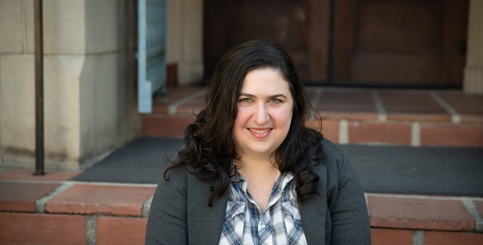 A portrait of Lisa Ruth Rand. She sits upon brick steps in a doorway.