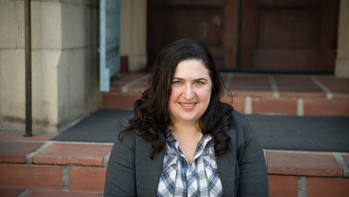 A portrait of Lisa Ruth Rand. She sits upon brick steps in a doorway.