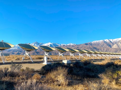 An array of radio dishes with snow covered mountains in background.