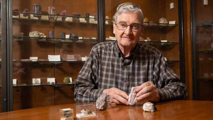 George Rossman in his office, in front of mineral samples on a wooden table.