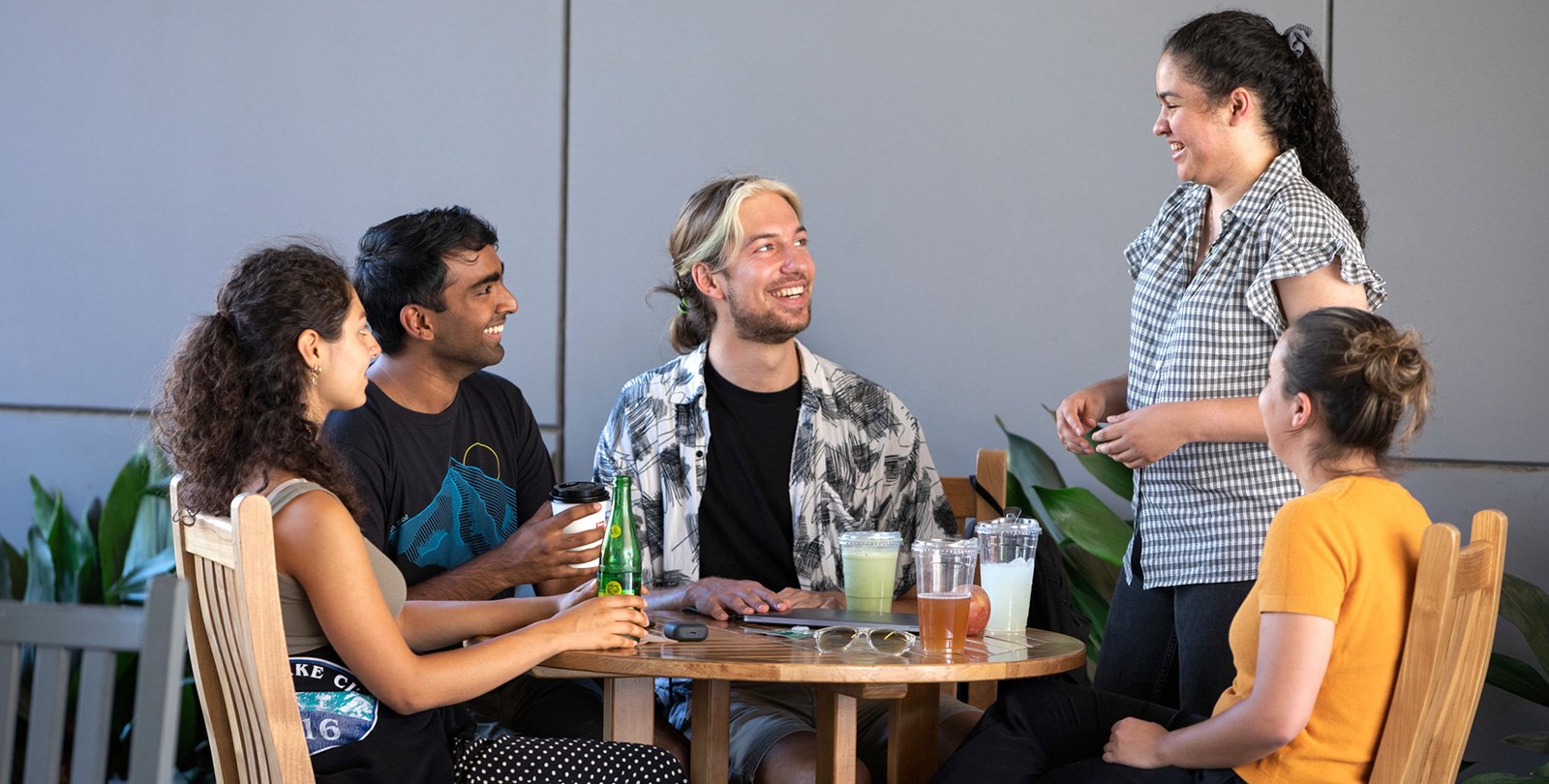 five students sit around a table talking and drinking beverages