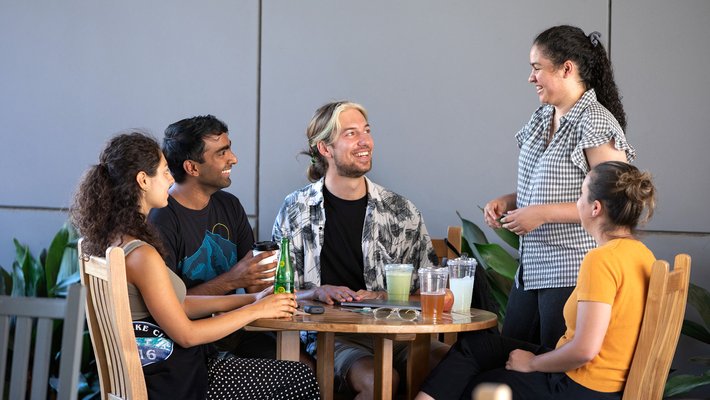 five students sit around a table talking and drinking beverages