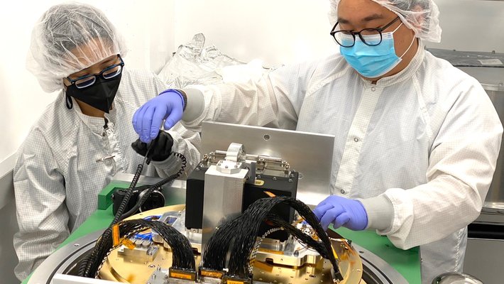 Scientists working on an instrument in lab, wearing protective suits.