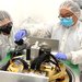 Scientists working on an instrument in lab, wearing protective suits.