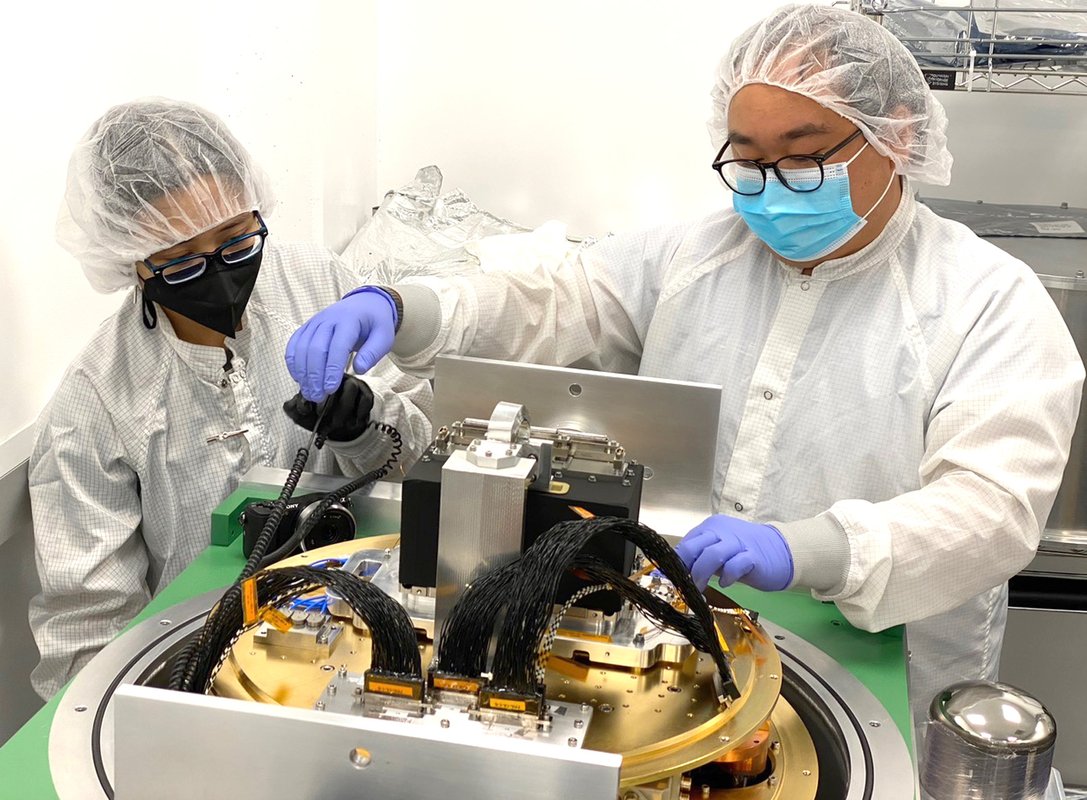 Scientists working on an instrument in lab, wearing protective suits.