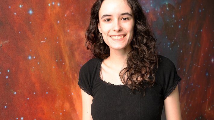 Sandra O'Neill wearing a black shirt and jeans, standing in front of an image of outer space